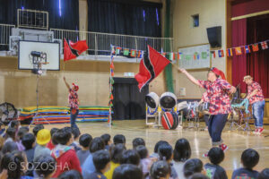 二人の演奏者がトリニダード・トバゴの旗を振りながら、スティールパンのリズムに合わせて舞う。観客の子どもたちの歓声が体育館を包む。 | 芸術鑑賞会・音楽鑑賞会 | スティールパン・コンサート |ワンハーツ・スチール・バンド | ONE HARTZ STEEL BAND |