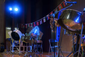 青い照明に照らされ、並べられたスティールパンと装飾されたステージセットのクローズアップ。 | 芸術鑑賞会・音楽鑑賞会 | スティールパン・コンサート |ワンハーツ・スチール・バンド | ONE HARTZ STEEL BAND |