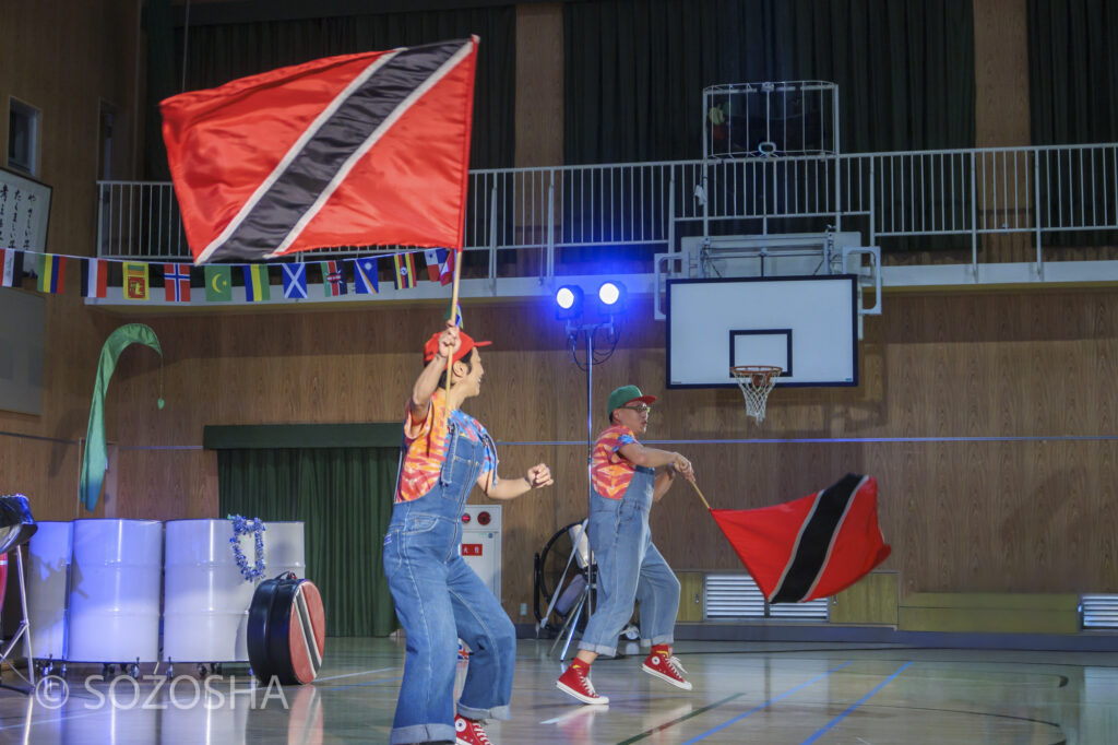 旗を振りながらステージを盛り上げる演奏者 | 芸術鑑賞会・音楽鑑賞会 | スティールパン・コンサート |ワンハーツ・スチール・バンド | ONE HARTZ STEEL BAND |