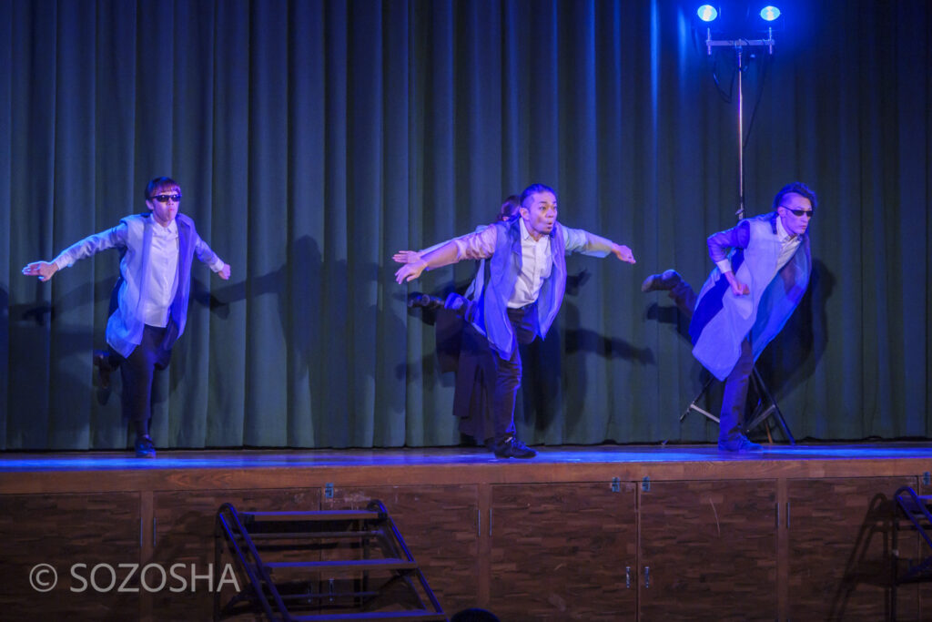 青い照明の中、俳優たちがマイムで水中を泳ぎ追いかけっこをしている。鳥のように腕を広げてバランスをとるマイムの場面。 | 芸術鑑賞会 | パントマイム |マイムボックス〜おしゃべりなカラダ〜 | いいむろなおき