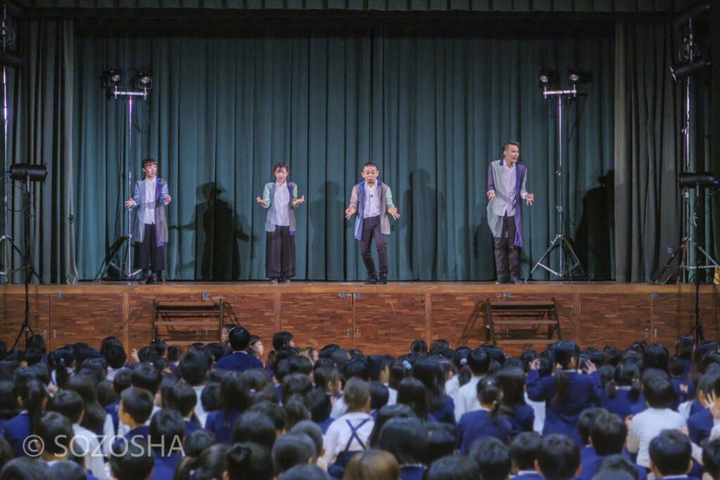 広い体育館で、4人の俳優がステージに並び、満席の児童たちに語りかけるようにマイム体験教室の進行している | 芸術鑑賞会 | パントマイム |マイムボックス〜おしゃべりなカラダ〜 | いいむろなおき