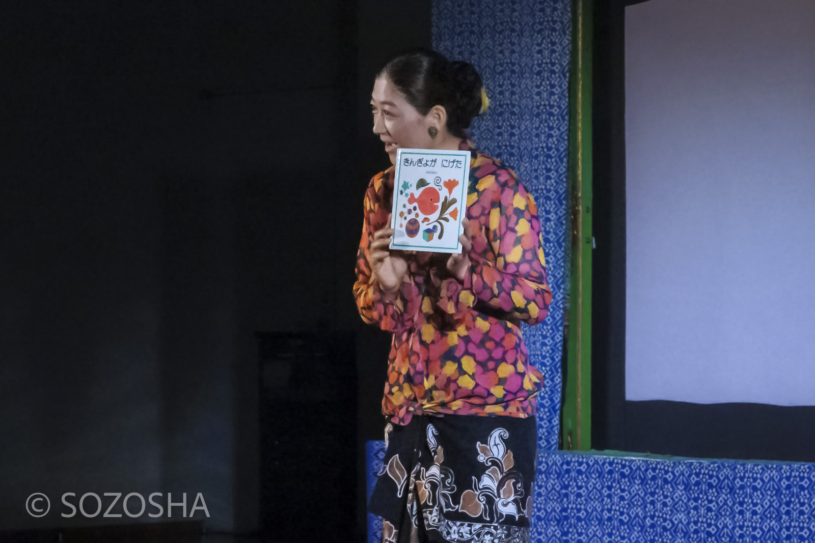 佐々木宏実が絵本「きんぎょがにげた」を紹介しながら、影絵の舞台へ案内している様子