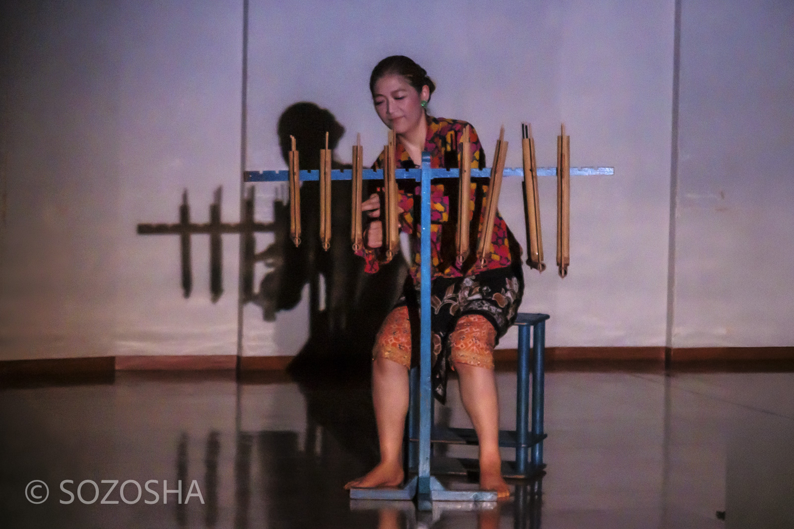 影絵音楽団くぷくぷの佐々木宏実が、インドネシアの竹楽器アンクルンを演奏し、影が壁に映っている様子